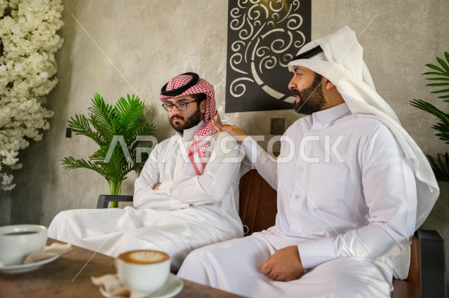 Saudi friends sitting in a cafe , a sad youth man with his friend , saudi man consoles his friend 