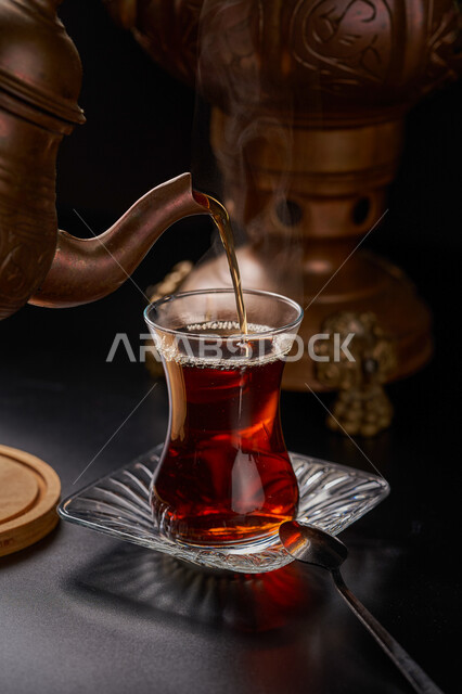 تقديم الشاي بالطريقة التقليدية في المملكة العربية السعودية, الاستمتاع بتناول المشروبات الساخنة, صورة مقربة لكوب من الشاي اللذيذ, خلفية الأواني النحاسية