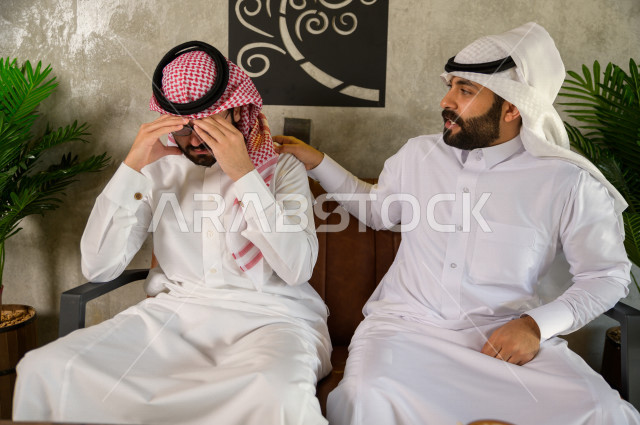 شابان عربيان سعوديان يجلسان في المقهى , احدهم يشعر بالحزن والاخر يقوم بمواساة صديقه , شاب عربي حزين , 