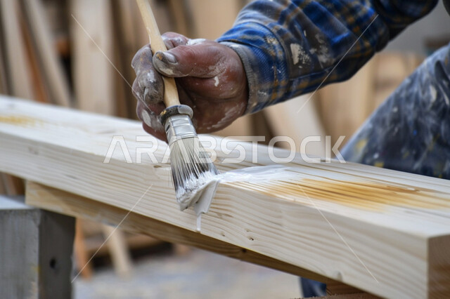 حرف ومهن يدوية شعبية، ورشات العمل في المملكة العربية السعودية، مهنة النجارة التقليدية، صورة مقربة ليد حرفي ماهر يقوم بوضع الطلاء على القطعة الخشبية، معامل تصنيع الأثاث الخشبي للمنازل