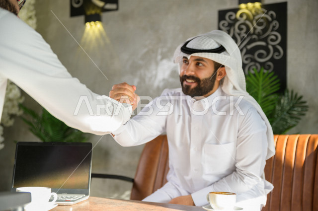 زملاء سعوديون يتقابلون في المقهى  ويتصافحون بابتسامه ,شاب سعودي يسلم على صديقه في المقهى ,تحية سعودية , مقابلة زملاء