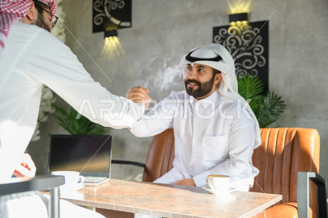 زملاء سعوديون يتقابلون في المقهى  ويتصافحون بابتسامه ,شاب سعودي يسلم على صديقه في المقهى ,تحية سعودية , مقابلة زملاء