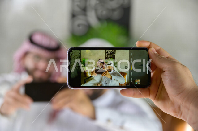  صديقان سعوديان يستعدان لالتقاط صورة تذكارية , صورة تذكارية شبابية , تصوير لحظات داخل المقهى , يد تمسك هاتف لتصوير شباب أصدقاء 