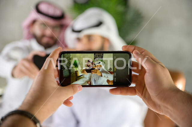 صديقان سعوديان يستعدان لالتقاط صورة تذكارية , صورة تذكارية شبابية , تصوير لحظات داخل المقهى , يد تمسك هاتف لتصوير شباب أصدقاء 