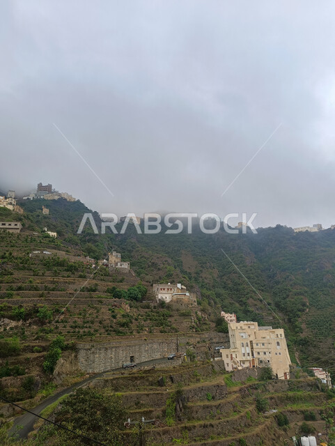  الأشجار والنباتات الخضراء المزروعة على سفوح الجبال, الاستمتاع بالمناظر الطبيعية في الأماكن السياحية في المملكة العربية السعودية، الغيوم والأجواء الضبابية فوق القمم والمرتفعات الجبلية في محافظة فيفاء، المدرجات الزراعية والبيوت والمباني السكنية في مدينة جازان