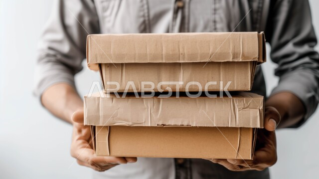 عمليات الشحن الموثوقه, خدمات التوصيل السريع, بورتريه مقرب لمندوب عربي سعودي خليجي يحمل بيده صناديق كرتونية، العمل في توصيل الطلبات والبضائع للزبائن والعملاء, التسوق الالكتروني الآمن, استلام طلبات الاونلاين, خلفيه بيضاء