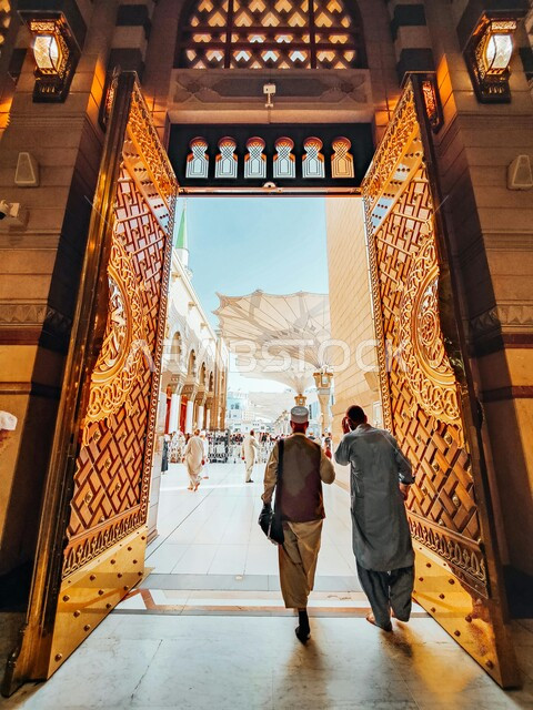صورة من الخلف لرجلان مسلمان يمران عبر بوابة المسجد النبوي الشريف،  العبادة والتقرب الى الله، معالم وأماكن دينية مقدسة في السعودية، ديكورات وتصاميم داخلية على الطراز الاسلامي، الزخارف الإسلامية الفخمة في المساجد