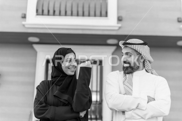 زوجان سعويان سعيدان، ينظر كل منهما للأخر بايماءات وجه  تدل على السعادة و الفرح و النصر بامتلاك منزل جديد سويا ، اسقرار العائلة ، امتلاك بيت جديد ، منازل و عقارات