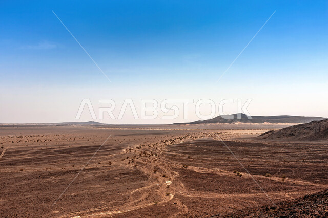 Dormant volcanic fields, Harrat Kashab field in the holy city of Mecca during the day, attractions for geotourism in the Kingdom of Saudi Arabia, desert environment and golden sand in front of volcanoes