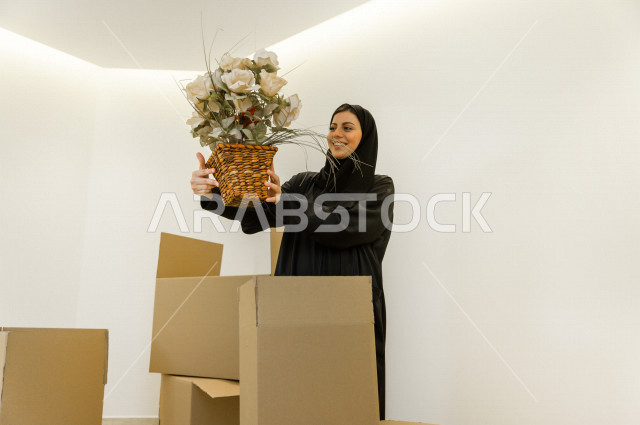 مرأه عربية سعودية  داخل منزلها الجديد ، تقوم بتفريغ محتويات الصناديق ،امتلاك بيت جديد ،ايماءات وجه و يدين تدل على السعادة والانسجام ، الترتيب و التنظيم ، النقل و التوصيل  