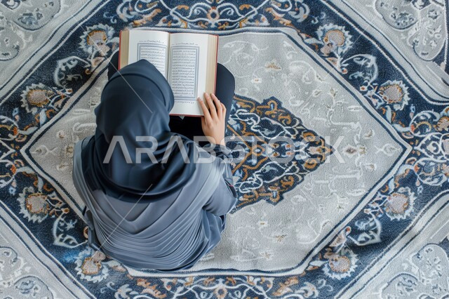 مفهوم الطمأنينه والخشوع، تلاوة وقراءة القرآن الكريم، صورة من الاعلى لإمرأة عربية سعودية خليجية ترتدي الحجاب والعباءة تجلس على سجادة الصلاة تحمل بيدها المصحف الشريف، الإكثار من ذكر الله تعالى والإجتهاد في العباده، التقرب الى الله في شهر رمضان