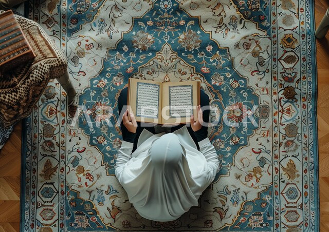 تلاوة وقراءة القرآن الكريم، مفهوم الطمأنينه والخشوع، صورة من الاعلى لإمرأة عربية سعودية خليجية ترتدي الحجاب والعباءة تجلس على سجادة الصلاة تحمل بيدها المصحف الشريف، الإكثار من ذكر الله تعالى والإجتهاد في العباده، التقرب الى الله في شهر رمضان
