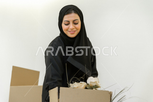 مرأه عربية سعودية  داخل منزلها الجديد ، تقوم بتفريغ محتويات الصناديق ،امتلاك بيت جديد ،ايماءات وجه و يدين تدل على السعادة والانسجام ، الترتيب و التنظيم ، النقل و التوصيل  
