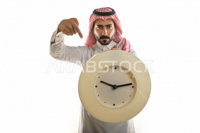بورتريه لرجل سعودي خليجي  سعيد بإيماءات الوجه المختلفة  ، تعابير وجه و يدين مختلفة  ، يحمل بيده ساعة حائط  ، يشير اصبعه الى الساعة ،خلفية بيضاء