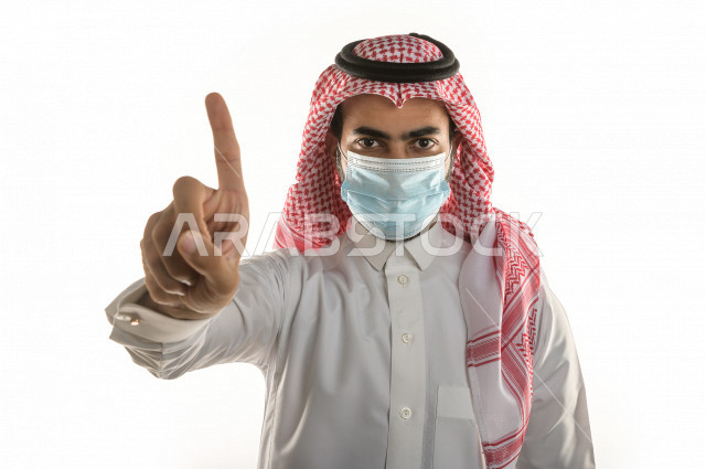 بورتريه لشاب سعودي يرتدي الكمامة ، يرفع يده ليتجنب المصافحة واقتراب الاخرين منه ، تجنب انتشار العدوى ، الحفاظ على المسافات ، خلفية بيضاء
