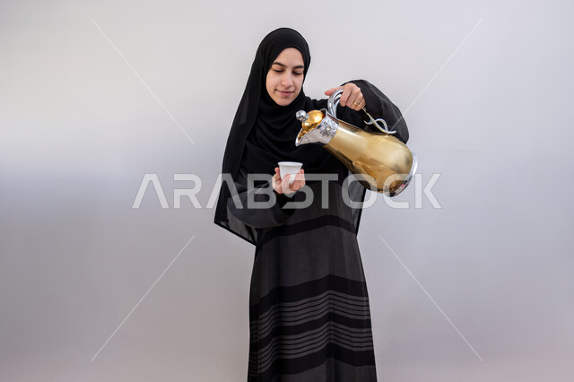  أصالة عادات وتقاليد المجتمع السعودي في المناسبات الاسلامية, كرم الضيافة وحسن الاستقبال في السعودية, بورتريه لشابة عربية خليجية سعودية مبتسمة ترتدي العباءة والحجاب تقوم بصب القهوة الخليجية, تقديم القهوة  العربية الأصيلة في الأعياد, خلفية بيضاء