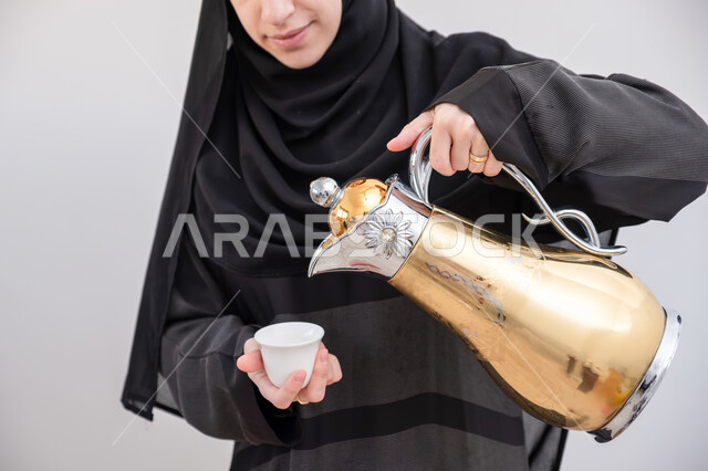  أصالة عادات وتقاليد المجتمع السعودي في المناسبات الاسلامية, كرم الضيافة وحسن الاستقبال في السعودية, بورتريه مقرب لشابة عربية خليجية سعودية مبتسمة ترتدي العباءة والحجاب تقوم بصب القهوة الخليجية, تقديم القهوة  العربية الأصيلة في الأعياد, خلفية بيضاء