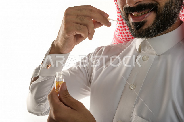 بورتريه لرجل عربي سعودي يختبر تولة من زيت العود العطري الفاخر على الجلد  ، العود العربي السعودي ، استخدام دهن العود في المناسبات الاجتماعية و المناسبات الدينية ،  اصالة العادات و التقاليد في المملكة العربية السعودية ، التطيب و التعطر