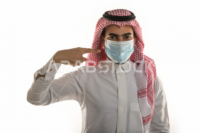 بورتريه لشاب سعودي يقوم بوضع الكمامة ، اتباع اجراءات السلامة بوضع الكمامة بشكل صحيح ، تجنب انتشار العدوى ، خلفية بيضاء