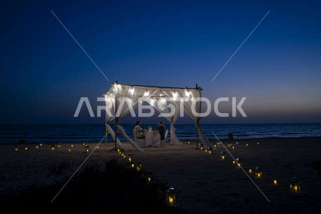 الجلسات واللحظات الرومانسية المليئة بالحب, الواجهة البحرية على ساحل البحر الأحمر, زوجان عربيان خليجيان سعوديان يستمتعان بتناول العشاء على شاطئ جزيرة فرسان في مدينة جازان في المملكة العربية السعودية في الغروب, معالم و أماكن سياحية مشهورة