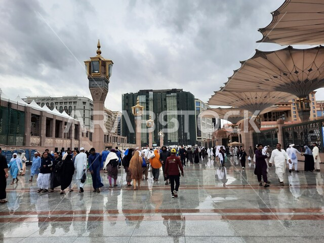 Muslims gathered in the outer courtyard of the Prophet’s Mosque in Medina, places for performing worship and religious duties, view of the sky filled with white clouds, worship and drawing closer to God Almighty, famous Islamic landmarks in Saudi Arabia, modern electronic umbrellas in the outer complex
