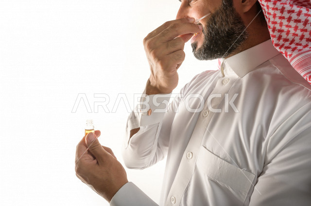 بورتريه لرجل عربي سعودي يختبر تولة من زيت العود العطري الفاخر على الجلد  ، العود العربي السعودي ، استخدام دهن العود في المناسبات الاجتماعية و المناسبات الدينية ،  اصالة العادات و التقاليد في المملكة العربية السعودية ، التطيب و التعطر