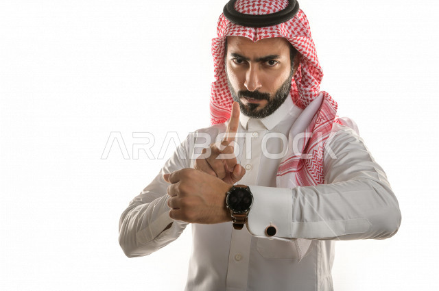 بورتريه لرجل سعودي خليجي  سعيد بإيماءات الوجه المختلفة  ، تعابير وجه و يدين مختلفة  ، يرتدي ساعة يد فاخرة  ، يشير اصبعه الى الساعة ،خلفية بيضاء
