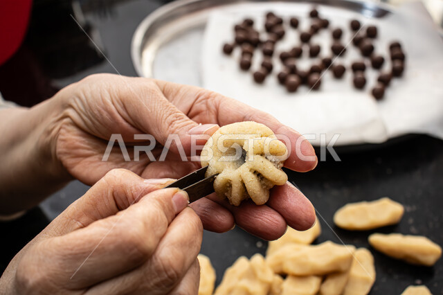 صورة مقربة ليد إمرأة تقوم بتشكيل قرص المعمول، طريقة إعداد وتحضير الحلويات الشهية، الاستعداد لاستقبال الأعياد والمناسبات الإسلامية السعيدة، قطع معمول العيد الشهية، كرم الضيافة وحسن الاستقبال في السعودية, منتجات محلية وطنية، حلى سعودي بالعجوة والمكسرات