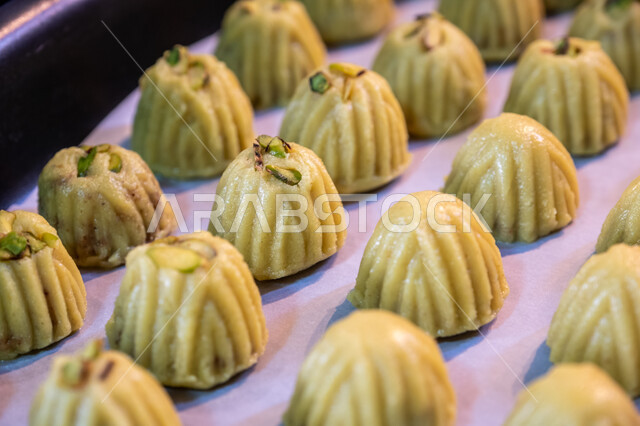 Preparing to receive happy Islamic holidays and occasions, pistachio maamoul tablets, Saudi sweets with nuts, how to prepare and prepare delicious sweets, delicious Eid maamoul pieces, warm hospitality and warm reception in Saudi Arabia, national local products.