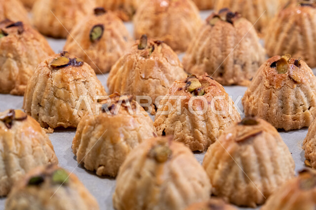 الاستعداد لاستقبال الأعياد والمناسبات الإسلامية السعيدة، قطع معمول العيد الشهية، كرم الضيافة وحسن الاستقبال في السعودية, منتجات محلية وطنية، وضع أقراص المعمول بالعجوة والمكسرات في الصواني، حلى سعودي تقليدي، طريقة إعداد وتحضير الحلويات الشهية