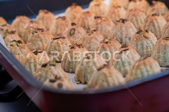 الاستعداد لاستقبال الأعياد والمناسبات الإسلامية السعيدة، قطع معمول العيد الشهية، كرم الضيافة وحسن الاستقبال في السعودية, منتجات محلية وطنية، وضع أقراص المعمول بالعجوة والمكسرات في الصواني، حلى سعودي تقليدي، طريقة إعداد وتحضير الحلويات الشهية