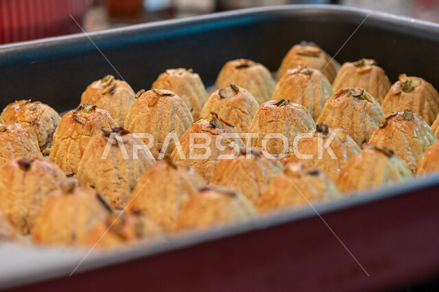 الاستعداد لاستقبال الأعياد والمناسبات الإسلامية السعيدة، قطع معمول العيد الشهية، كرم الضيافة وحسن الاستقبال في السعودية, منتجات محلية وطنية، وضع أقراص المعمول بالعجوة والمكسرات في الصواني، حلى سعودي تقليدي، طريقة إعداد وتحضير الحلويات الشهية