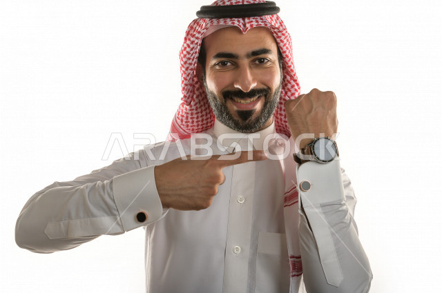 بورتريه لرجل سعودي خليجي  سعيد بإيماءات الوجه المختلفة  ، تعابير وجه و يدين مختلفة  ، يرتدي ساعة يد فاخرة  ، يشير اصبعه الى الساعة ،خلفية بيضاء