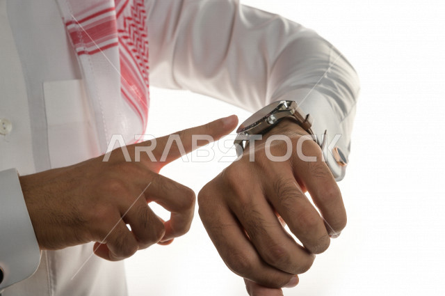بورتريه لرجل سعودي خليجي  سعيد بإيماءات الوجه المختلفة  ، تعابير وجه و يدين مختلفة  ، يرتدي ساعة يد فاخرة  ، يشير اصبعه الى الساعة ،خلفية بيضاء
