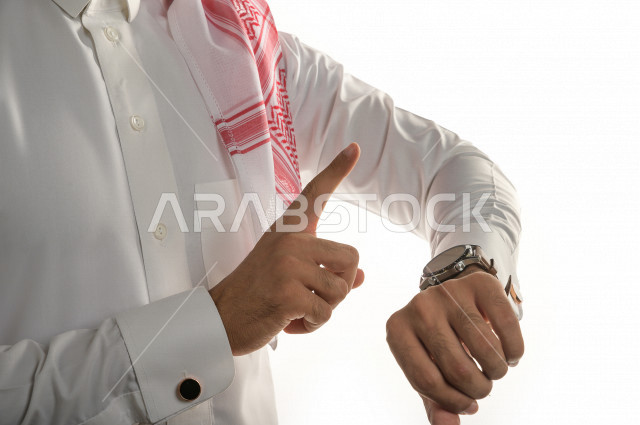 بورتريه لرجل سعودي خليجي  سعيد بإيماءات الوجه المختلفة  ، تعابير وجه و يدين مختلفة  ، يرتدي ساعة يد فاخرة  ، يشير اصبعه الى الساعة ،خلفية بيضاء