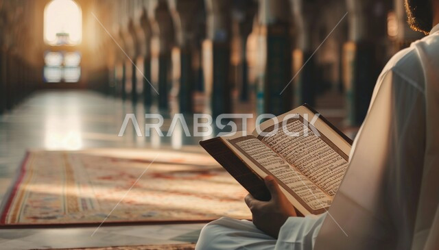 The architectural art of mosques, recitation and chanting of the Book of God, a spiritual religious atmosphere, worship and closeness to God, a close-up picture from the side of a Saudi Gulf Arab man wearing the traditional dress sitting inside a mosque reading the Qur’an