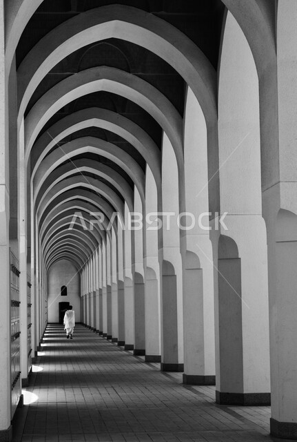 الأقواس والأعمدة بديكورات وتصاميم داخلية على الطراز الاسلامي، صورة من الخلف لرجل عربي خليجي سعودي مسلم يرتدي لباس الحرام يسير في مسجد بير علي في المدينه المنوره, العبادة والتقرب الى الله، أماكن ومعالم دينية مقدسة في السعودية