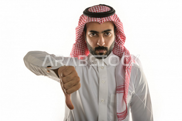 بورتريه لرجل سعودي خليجي غاضب و عابس بإيماءات وجه و يدين مختلفة  ، تعابير وجه و يدين مختلفة , يشير اصبع الإبهام الى الأسفل  ، خلفية بيضاء
