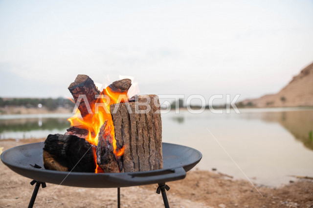 موقد نار مشتعل في احدى الرحلات البرية في صحراء المملكة العربية السعودية في وقت شروق الشمس ، اجواء بريه ممتعة في مناطق صحراوية سياحية ، جمال الطيعية السعودية ، البر و التخييم 