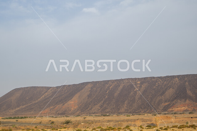 القمم والمرتفعات والتضاريس في الضواحي، التكوينات الصخرية للجبال في المناطق الصحراوية للمملكة العربية السعودية، سلسلة جبلية بجانب طريق سفر سريع في النهار