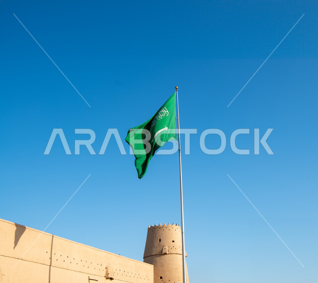 الهندسة المعمارية والمباني الطينية القديمة من التراث السعودي، أماكن ومعالم أثرية سياحية في السعودية، سارية العلم الوطني السعودي يرفرف بالسماء،  صورة مقربة لقصر المصمك التاريخي في مدينة الرياض في المملكة العربية السعودية