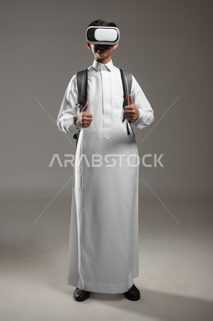 A study activity using virtual reality, simulating the imaginary world with expressions of admiration and satisfaction, a portrait of a Saudi Gulf Arab student wearing a traditional dress and a school backpack, wearing VR glasses, full body image, gray background, sensitive content, sensitive use