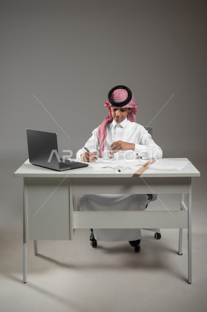 Gaining knowledge and experience with gestures of precision and focus, drawing an engineering design diagram, using modern technical devices in scientific fields, a portrait of a Saudi Arabian Gulf boy wearing a shemagh and traditional dress sitting in front of his computer using engineering tools and equipment, gray background, sensitive use, sensitive content