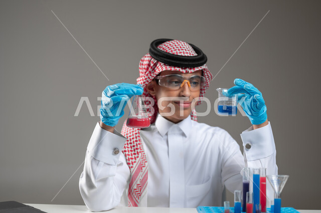 Gaining knowledge and experience with gestures of precision and concentration, development, research, and conducting chemical reactions, studies and experiments in an advanced practical environment, close-up portrait of a Saudi Gulf Arab student wearing traditional clothing, wearing goggles, sitting in front of the laptop doing a scientific experiment, gray background, sensitive content, sensitive use