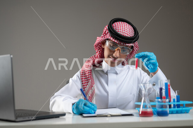 Studies and experiments in an advanced practical environment, gaining knowledge and experience with gestures of precision and concentration, development, research, and conducting chemical reactions, a close-up portrait of a Saudi Gulf Arab student wearing traditional clothing, wearing goggles, sitting in front of the laptop doing a scientific experiment, gray background, sensitive content, sensitive use