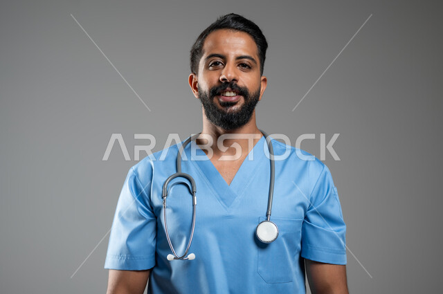 Preparing to provide services to patients with all efficiency, the concept of medicine and health care, standing ready and looking at the camera with happy gestures, a close-up portrait of a smiling Saudi Arabian Gulf nurse wearing a work uniform and wearing a stethoscope, gray background, sensitive content, sensitive use