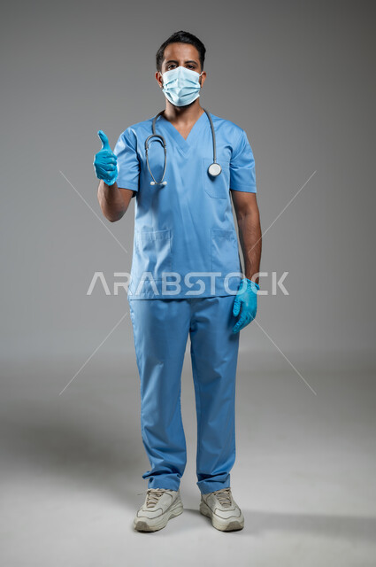 الرضا بجوده الخدمات الطبية، الالتزام بالاحترازات الوقائيه ضد كوفيد 19, بورتريه لممرض عربي سعودي خليجي يرتدي يونيفورم العمل يشير بإصبع الإبهام نحو الاعلى، ارتداء الكمامه لتجنب انتشار فايروس كورونا, الجسم بالطول الكامل, خلفية رمادية، محتوى حساس، استخدام حساس