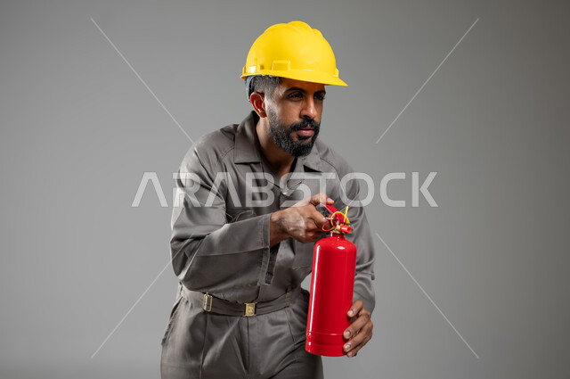 تعابير الاقتراب بحذر ,وظائف ومهن سعودية, مساعدة الناس والتطوع بعمليات الإنقاذ, المعدات اللازمة لإطفاء الحريق ،بورتريه لرجل عربي خليجي سعودي يرتدي سترة الحماية والخوذة يعمل في الدفاع المدني يحمل بيده مطفأة الحريق, خلفية رمادية, محتوى حساس, استخدام حساس