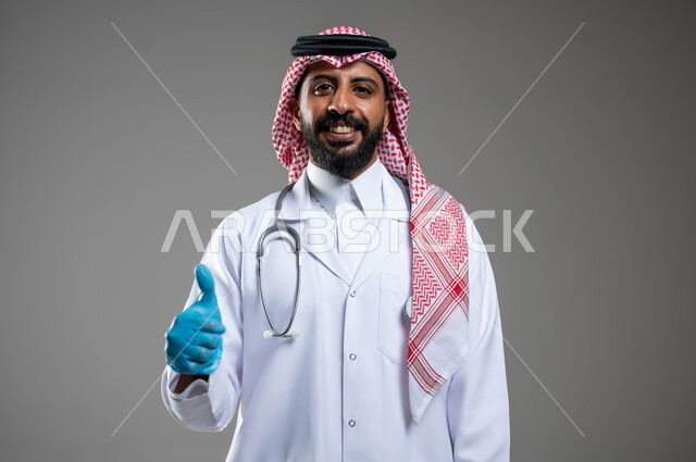 الرضا عن الخدمات الطبيه والرعاية الصحيه، إيماءات مختلفة تدل على علامات الجودة، بورتريه مقرب لطبيب عربي سعودي خليجي يرتدي الثوب مع المعطف الطبي والشماغ يرفع أصبع الأبهام بتعابير الاعجاب، خلفية رمادية، محتوى حساس، استخدام حساس