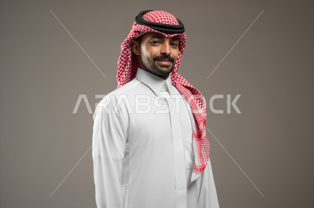 مفهوم الرجولة والقوة والثقة بالنفس، بورتريه مقرب حانبي لرجل عربي خليجي سعودي يرتدي الشماغ والثوب السعودي ينظر الى الكاميرا بإيماءات الجدية والحزم، الاهتمام بالأناقة والمظهر الخارجي، خلفية رمادية، محتوى حساس، استخدام حساس